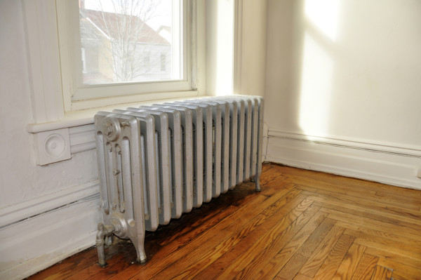 old heating radiator in an empty room by a window with a hardwood floor and white walls. [url=https://www.istockphoto.com/file_search.php?action=file&lightboxID=7367283]See more images in Heating and Cooling Lightbox [img]/file_thumbview_approve.php?size=1&id=11166157[/img] [/url]