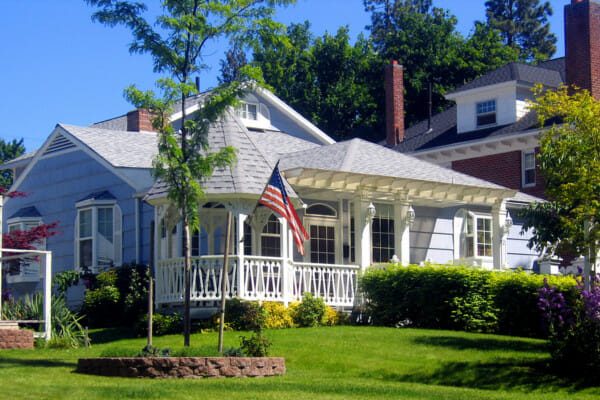 American curb appeal example with a beautiful white house with a flag out front and a rounded porch on one corner