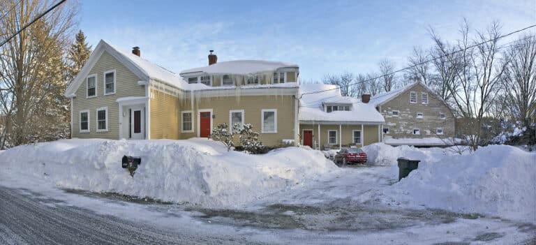 Massachusetts home showing severe ice dam formation and icicles along roof edge requiring immediate professional roof repair.
