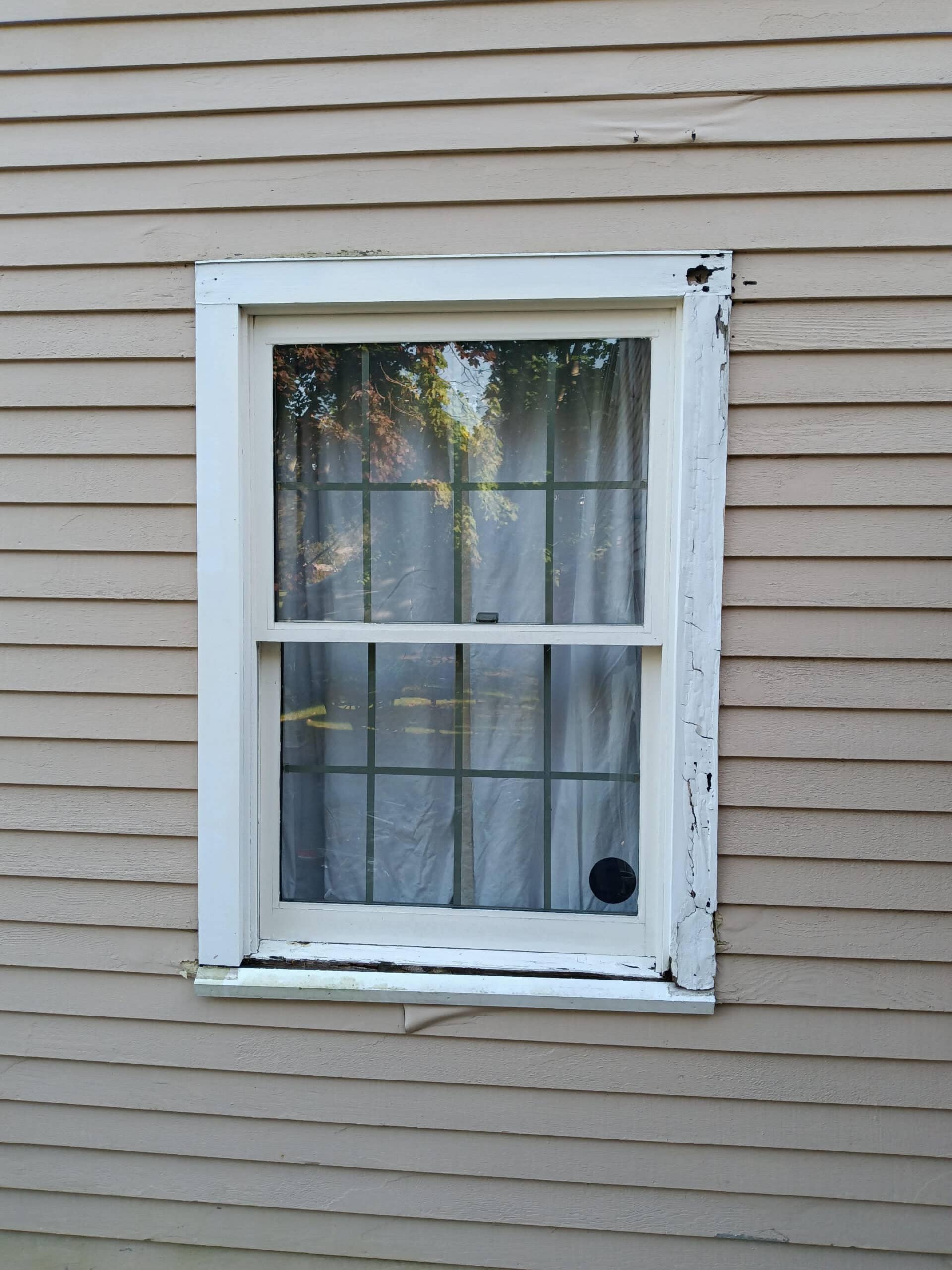 Old wood window with peeling paint and frame rot, showing signs of moisture damage and potential water leaks.