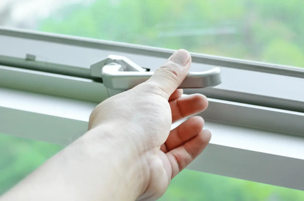A hand operates the handle on a modern casement window designed to close tightly and securely. One reason homeowners ask why do windows get foggy in summer is that failed seals can allow moisture between panes, while properly functioning hardware helps maintain a more reliable airtight fit.