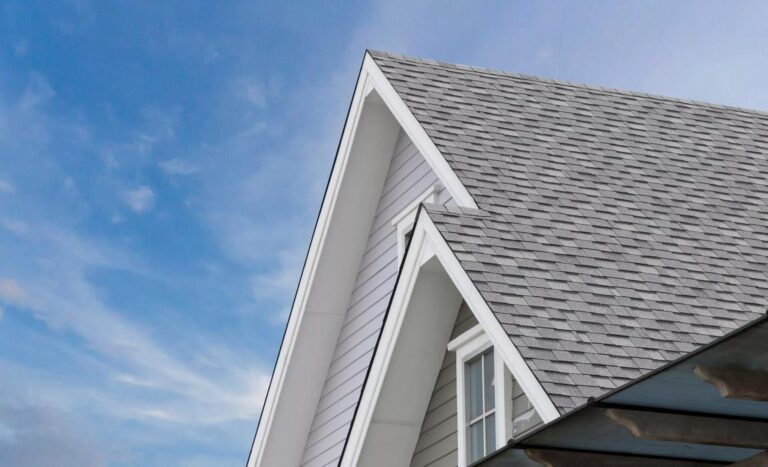 Close-up view of a house roof with gray asphalt shingles, white trim, and a clear blue sky—showcasing expert roofing in Danvers MA.