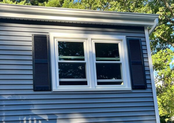 White replacement double-hung windows installed on gray vinyl siding home to improve energy efficiency in summer.