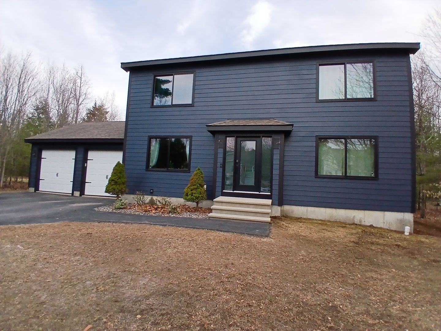 Deep blue fiber cement siding, black-framed windows, and a covered front entry give this Rochester, NH home a fresh, weather-ready exterior beside its two-car garage. Upgrades like this are featured in our ultimate fall home maintenance checklist.
