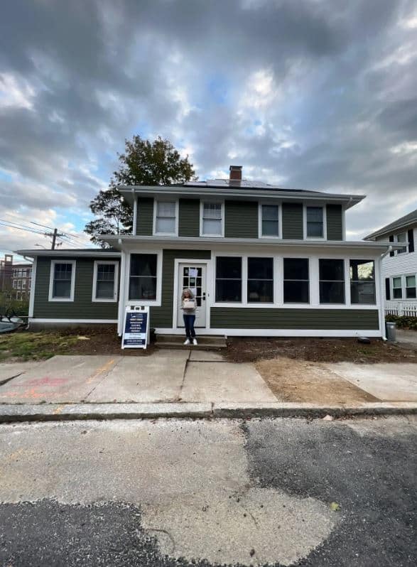 A person stands in front of a charming two-story green house with white trim in Beverly, MA