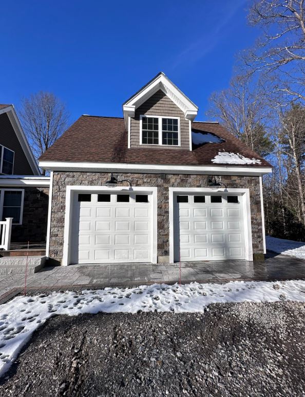 A two-car garage with a stone exterior and white doors under a clear blue sky in Tilton, NH