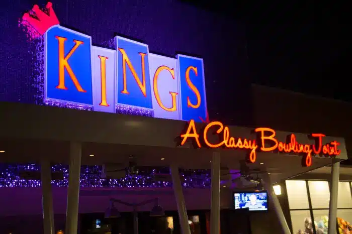 A brightly lit sign at night reads KINGS in large blue letters with a red crown, and below it, red neon letters spell A Classy Bowling Joint. The building in Lynnfield is illuminated, a popular spot for charity events and featured by NorthShore Magazine.