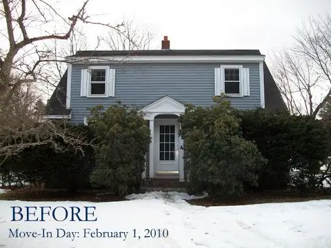 A two-story blue-gray house with white trim and striking window transformations stands among leafless trees and bushes behind a patchy snow-covered yard. Text reads BEFORE Move-In Day: February 1, 2010 in the lower left corner.