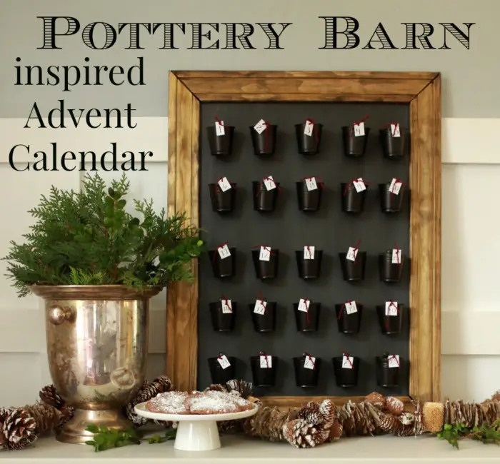 A framed Pottery Barn Inspired DIY advent calendar with 25 small black buckets, each numbered, hangs above a table adorned with greenery, pinecones, and cookies. Text reads “Pottery Barn inspired Advent Calendar.”.