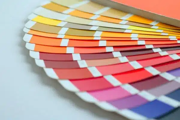A spread of color swatches in various shades of orange, red, and pink fanned out on a surface. The swatches display vibrant gradient hues for design or painting purposes.