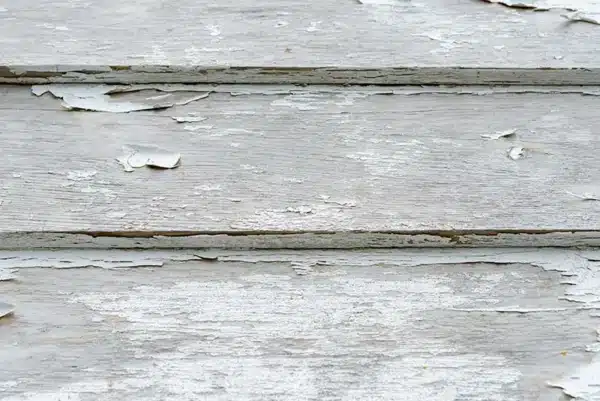 Peeling white paint on wooden planks reveals their age and weathering, showing a sharp contrast to the sleekness of insulated vinyl siding. The surface is rough and cracked with patches of exposed wood, telling tales of long exposure to harsh elements.