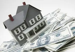 A small model house sits atop a scattered pile of U.S. dollar bills, symbolizing real estate investment, home renovation facts, or the cost of buying a home.