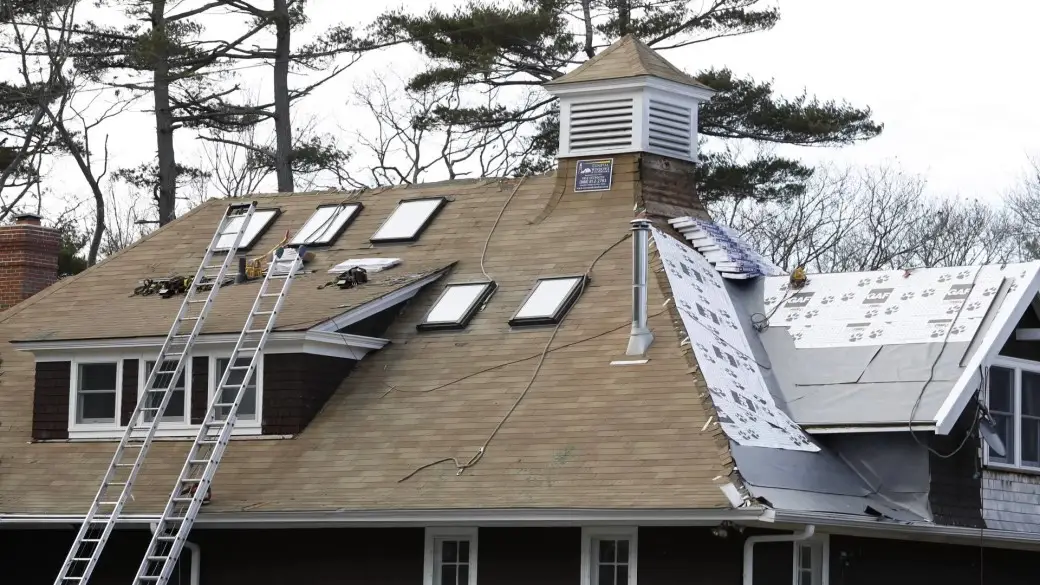 A house roof under construction, with ladders and tools on the shingles. Several skylights are installed, and part of the GAF Roof has underlayment exposed, ready for new shingles. Trees are visible in the background.