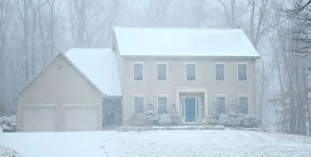A two-story house with an attached double garage is covered in snow during a polar vortex, as frigid temperatures sweep through and trees faintly appear in the snowy background.