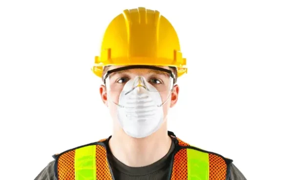 A construction worker wearing a yellow hard hat, safety glasses, a high-visibility vest, and a protective face mask stands against a white background, ready to work on exteriors for Coastal Windows projects.