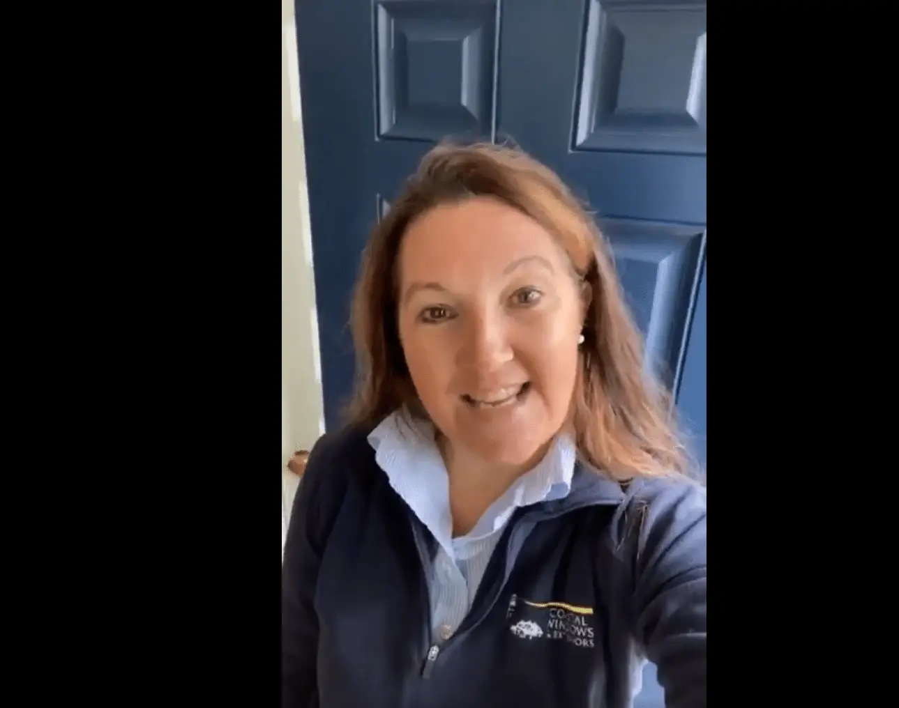 A person with long hair, perhaps Stephanie Vanderbilt, stands in front of a blue door, smiling at the camera. Clad in a dark blue jacket over a light blue collared shirt, their cheerful gaze seems to convey a warm message from the owner.