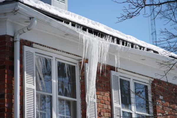 Icicles and ice dam buildup along roof edge showing why to Prevent and Remove from Your Roof.