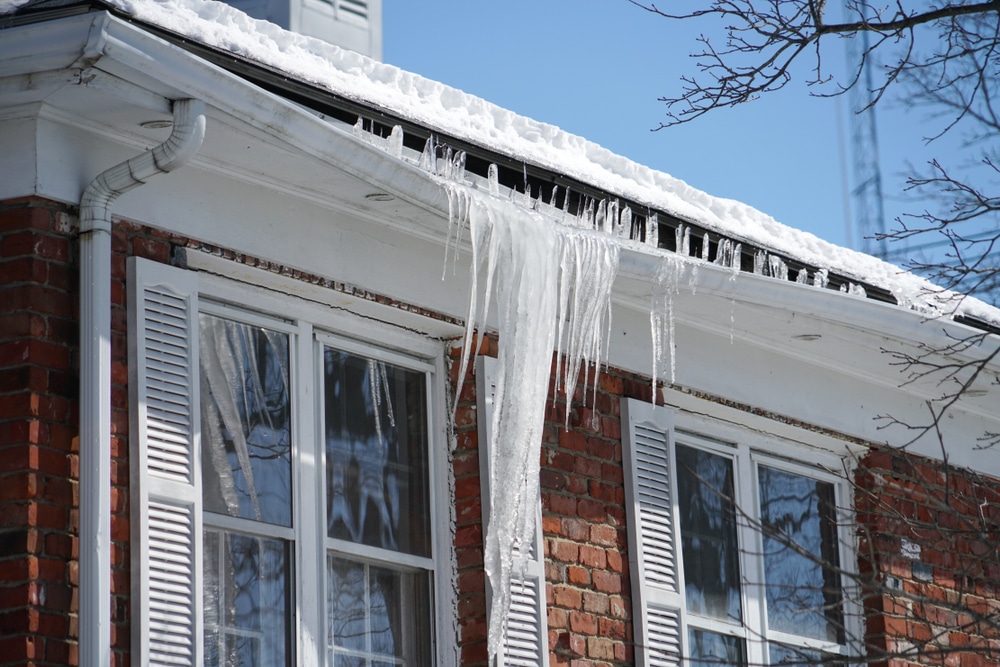 Icicles and ice dam buildup along roof edge showing why to Prevent and Remove from Your Roof.