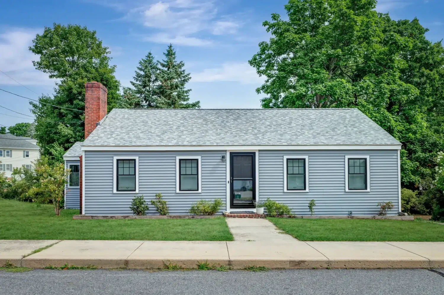 A finished Beverly home features gray siding, black-trimmed windows, a dark entry door, and a light asphalt shingle roof. This exterior demonstrates how a home maintenance checklist can cover roofing, siding, windows, doors, landscaping, and drainage around the entire property.