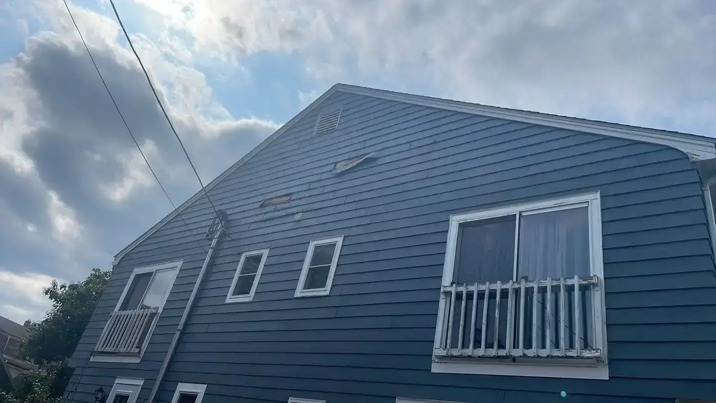 Older blue siding covers the broad gable wall of a Beverly home with several windows and exterior utility lines. A complete home maintenance checklist should include looking for loose panels, fading, warping, cracks, moisture stains, and openings around windows or vents.