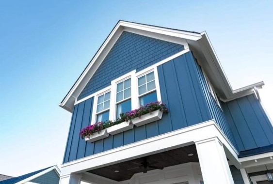 A modern blue house with white trim, Hardie Siding in Winchester MA, and elegant columns. Two upper windows feature a flower box filled with purple flowers, set against a clear blue sky.