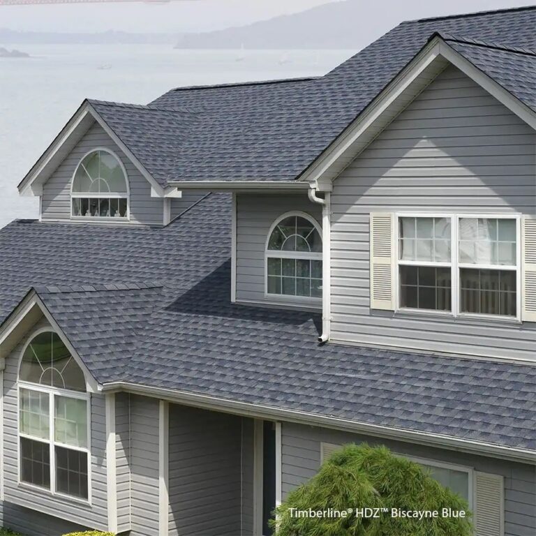 Architectural shingles cover the steep roof and dormers of this classic gray home with white trim. When shingles crack, loosen, or deteriorate, roof installation in Bristol NH restores dependable weather protection.