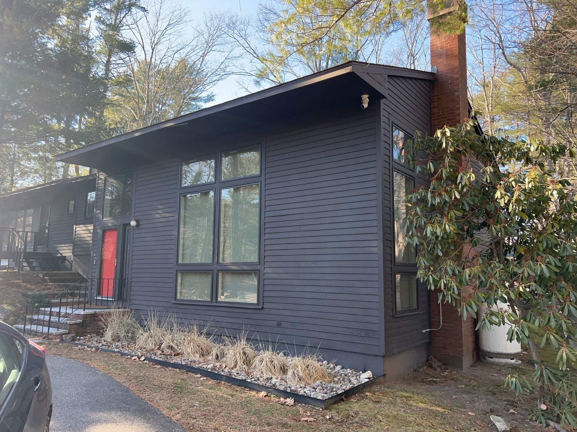 The front corner of the home shows weathered dark wood siding, tall windows, and dried ornamental grasses along the bed. James Hardie certified installers in Canton would replace this aging exterior.