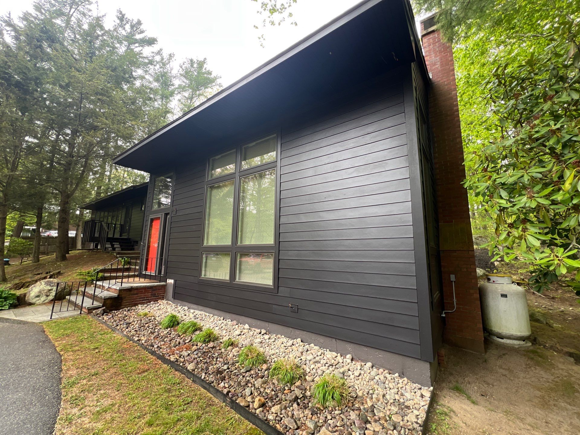 Gravel landscaping and new plantings line the base of this Canton home's front wing, finished in Midnight Black smooth plank beside a tall brick chimney. Factory-finished color from James Hardie certified installers in Canton means less upkeep.