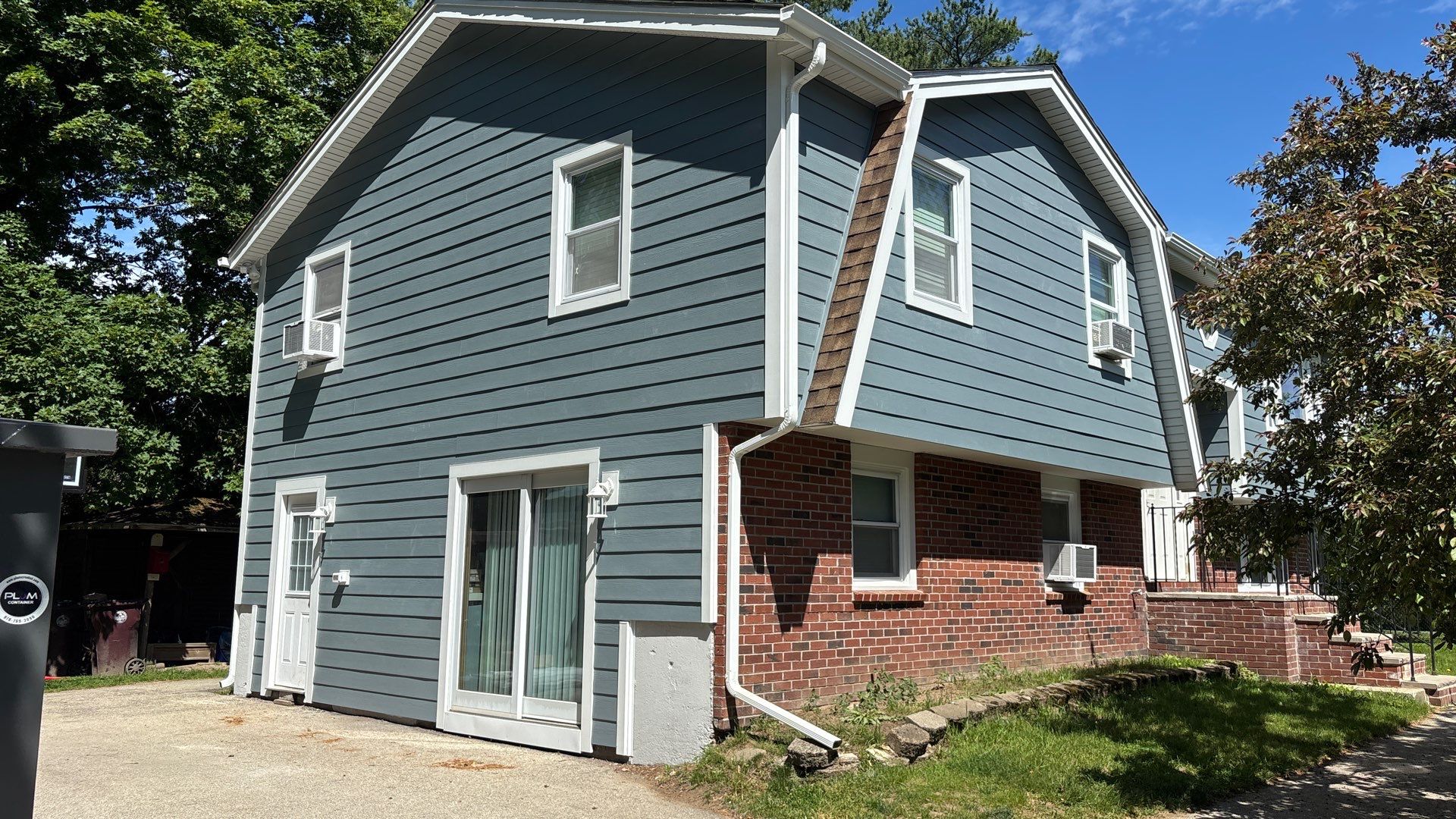 The side of this Lowell home now shows Boothbay Blue plank on both the gambrel-style upper wall and the lower level, with a white slider and entry door. James Hardie certified installers in Lowell trimmed every opening in Arctic White.