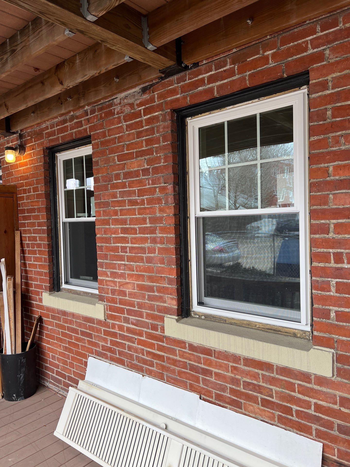 Along the porch, a pair of replacement windows with white frames and grids sits in the brick beside a stone sill, with old window parts removed below. Work in progress shows the care behind this window installation in Salem MA.