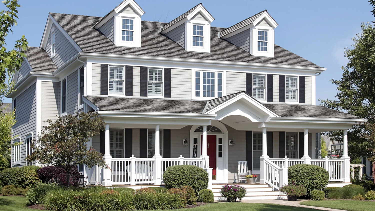 A gray Colonial-style home with a red front door and wraparound porch, representing exterior remodeling by Coastal Windows & Exteriors in Beverly, MA.