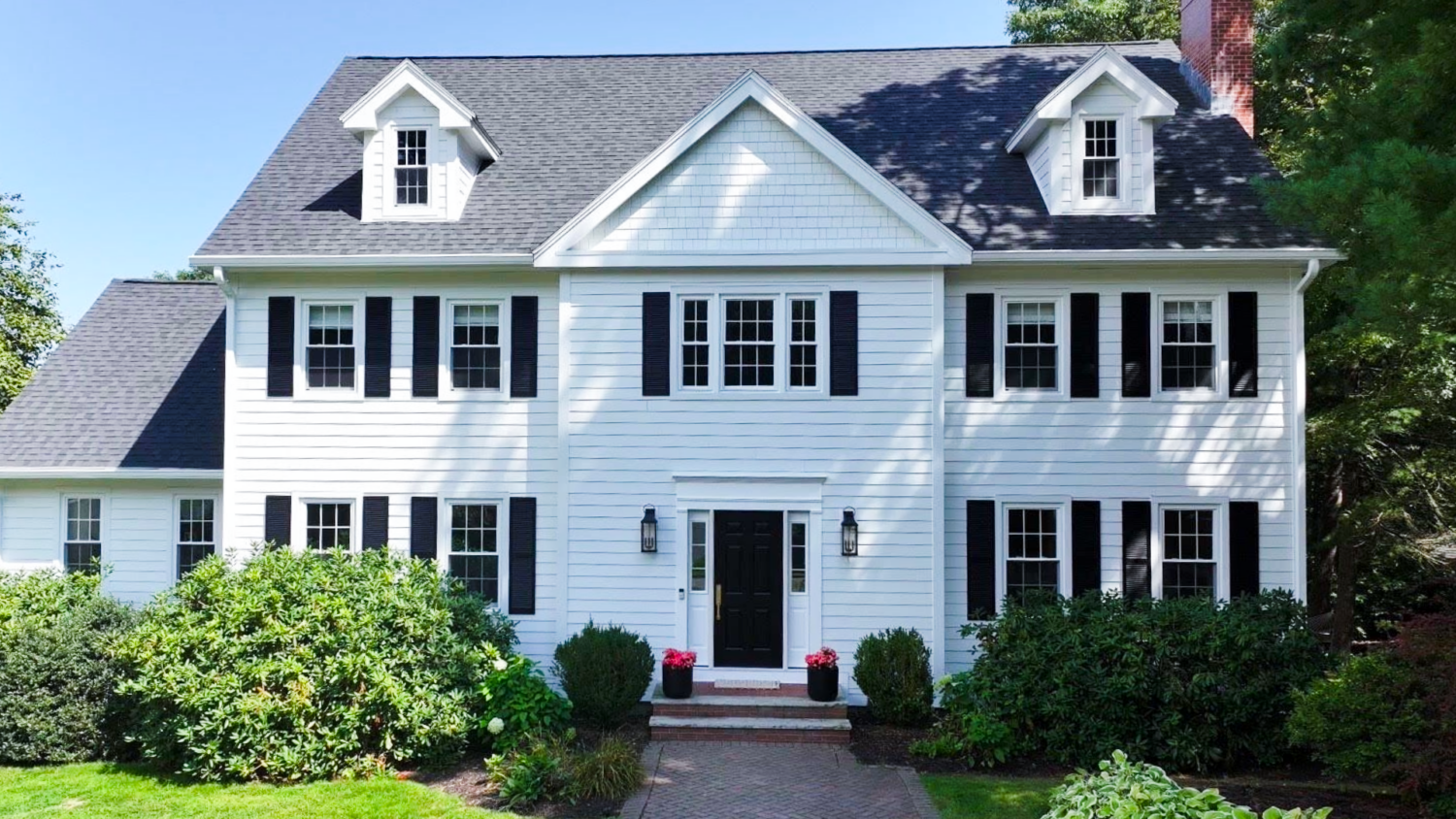 A white colonial-style home with black shutters, representing exterior remodeling work by Coastal Windows & Exteriors in Beverly, MA.