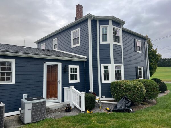 Navy-sided colonial with new white double-hung replacement windows in a corner bay and rear addition in Amesbury, North Shore.