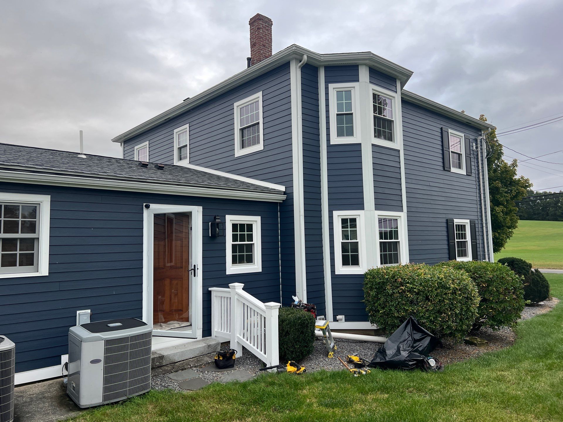 Navy-sided colonial with new white double-hung replacement windows in a corner bay and rear addition in Amesbury, North Shore.
