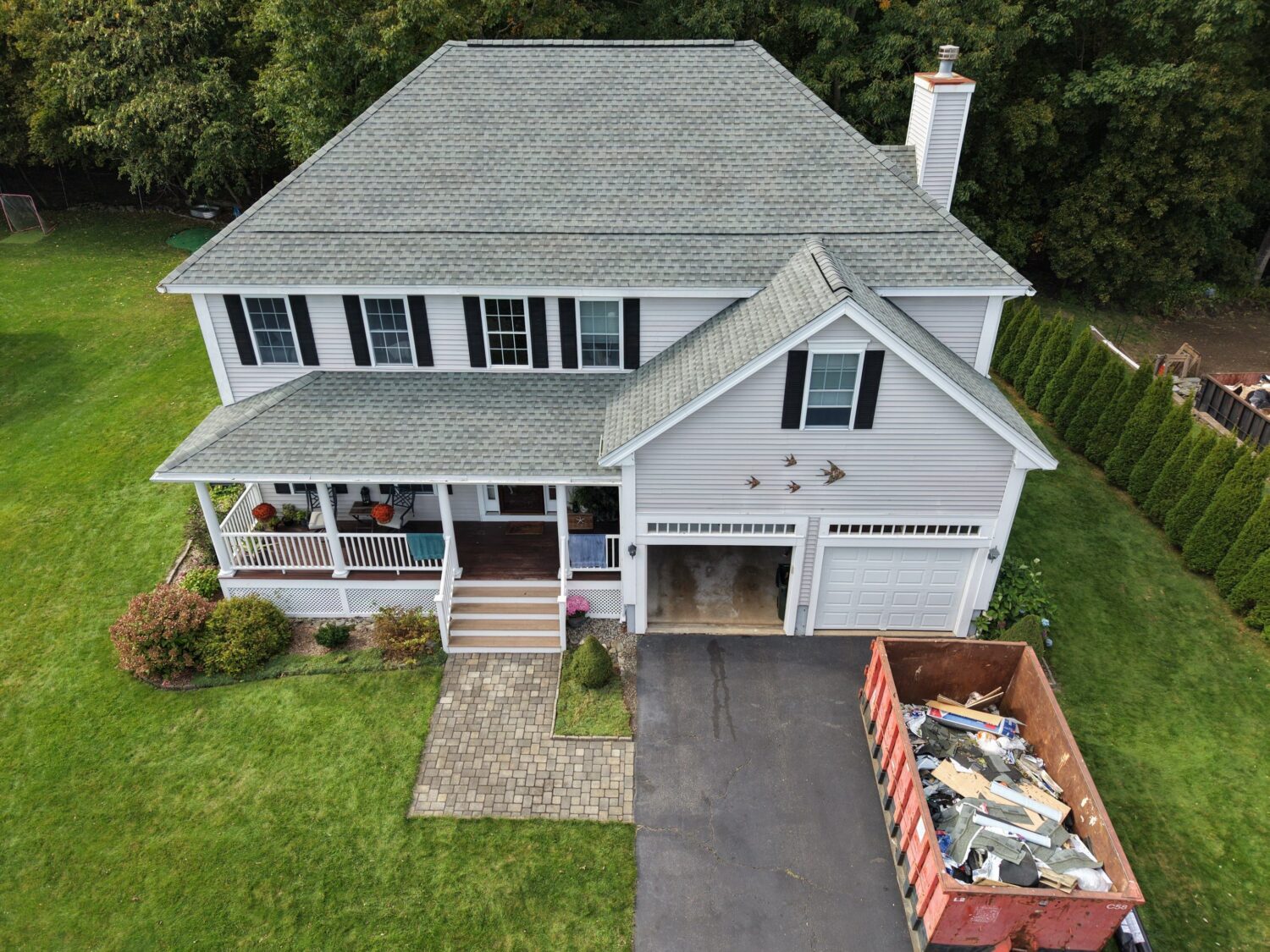 Aerial view of a Newburyport, MA home with a new gray shingle roof and a dumpster of tear-off debris in the driveway during a roof replacement.