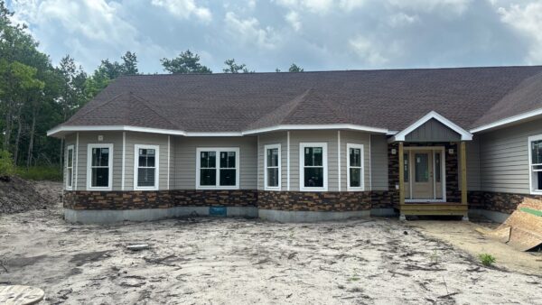 Twin bay windows trimmed in white rise above a warm brown Evolve Stone base, framed by greige CraneBoard lap siding on this Plymouth ranch. A board-and-batten gable caps the covered entry, finishing this siding installation in Plymouth.