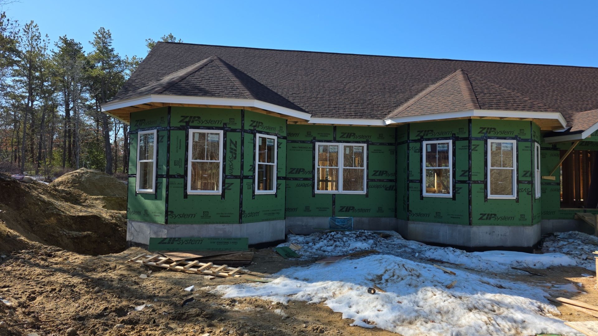 Green ZIP System sheathing wraps the twin bay windows of this new Plymouth ranch, with snow still on the ground and the roof already shingled. This was the starting point for the siding installation in Plymouth.